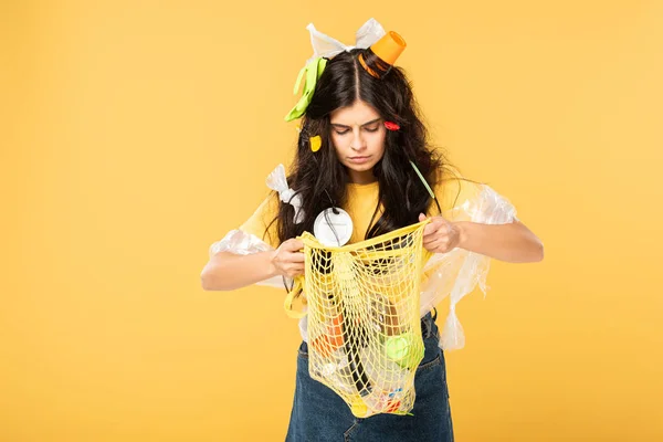 Frustrated woman with trash in hair holding bag with rubbish isolated on yellow — Stock Photo