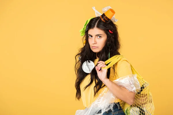 Upset girl with trash in hair holding bag with rubbish isolated on yellow — Stock Photo