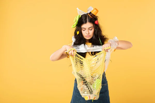 Emotional girl with trash in hair holding bag with rubbish isolated on yellow — Stock Photo