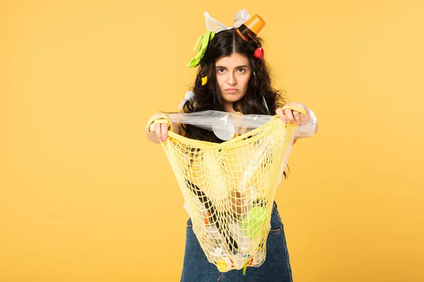 Confused girl with trash in hair holding bag with rubbish isolated on yellow — Stock Photo