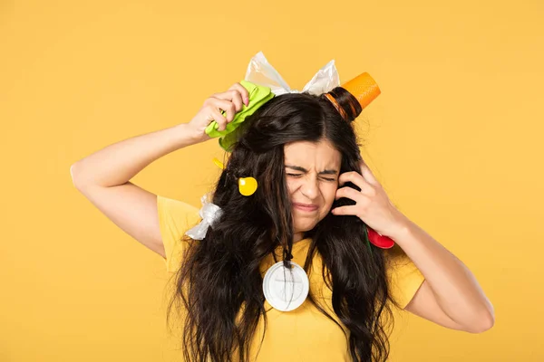 Worried young woman with rubbish in hair isolated on yellow — Stock Photo