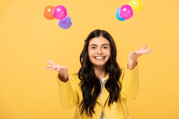 Красива усміхнена дівчина з різнокольоровими кульками, ізольована на жовтому — стокове фото