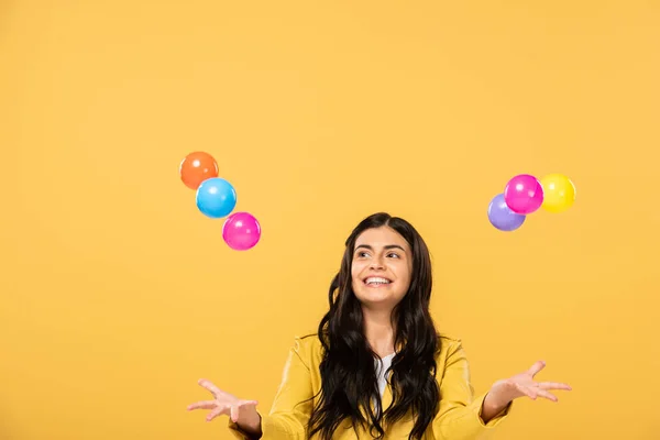 Збуджена брюнетка дівчина з різнокольоровими кульками, ізольована на жовтому — стокове фото