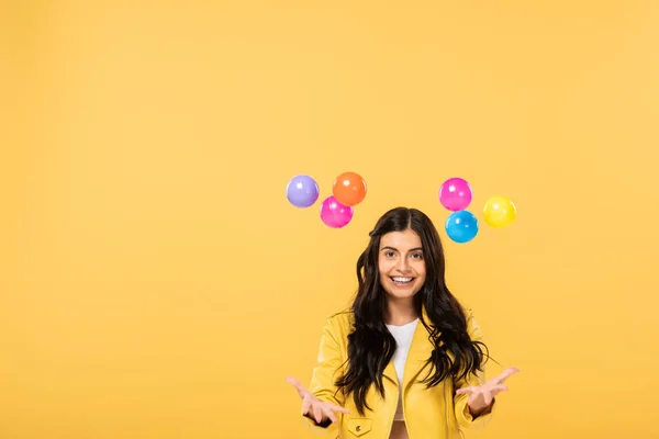 Atractiva chica sonriente con bolas de colores, aislado en amarillo - foto de stock