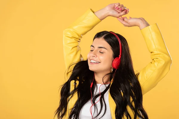 Belle femme gaie dansant et écoutant de la musique avec écouteurs, isolé sur jaune — Photo de stock