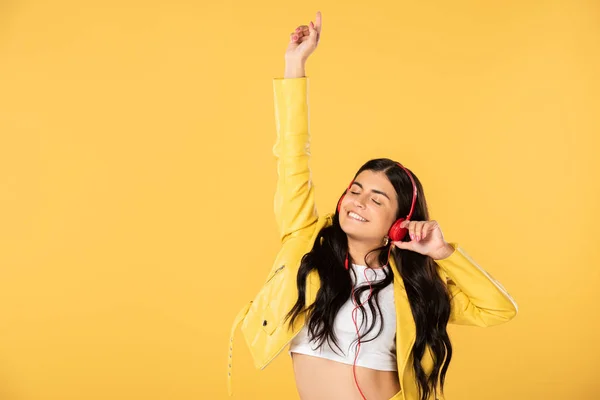 Chica morena bailando y escuchando música con auriculares, aislada en amarillo - foto de stock