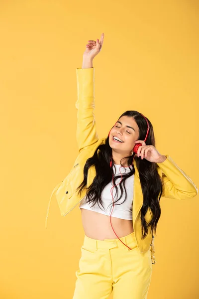 Chica feliz bailando y escuchando música con auriculares, aislado en amarillo - foto de stock