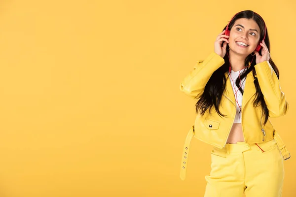 Симпатичная молодая женщина, слушающая музыку в наушниках, изолированная на желтом — стоковое фото