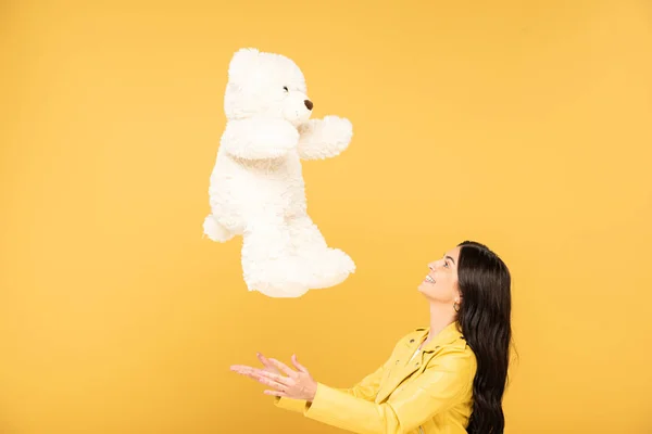 Hübsche junge Frau wirft Teddybär hoch, isoliert auf gelb — Stockfoto