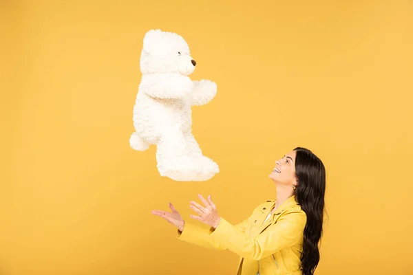 Attraktive Mädchen werfen Teddybär, isoliert auf gelb — Stockfoto