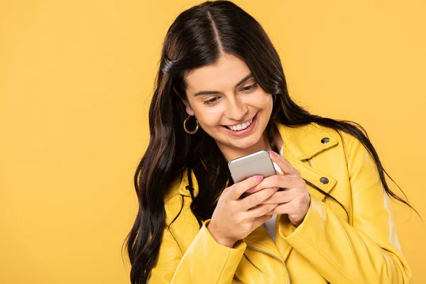 Привлекательная брюнетка девушка с помощью смартфона, изолированный на желтый — стоковое фото