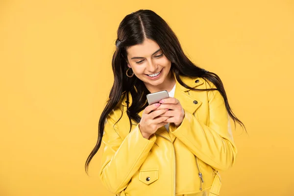 Alegre morena chica usando smartphone, aislado en amarillo - foto de stock