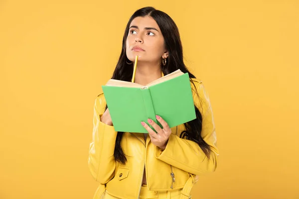 Красивый студент думает, держа карандаш и книгу, изолированные на желтый — стоковое фото