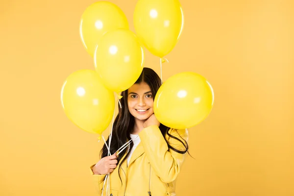 Chica feliz sosteniendo globos amarillos, aislado en amarillo - foto de stock