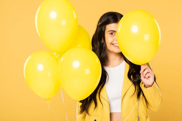 Joyeuse femme brune tenant des ballons jaunes, isolée sur jaune — Photo de stock