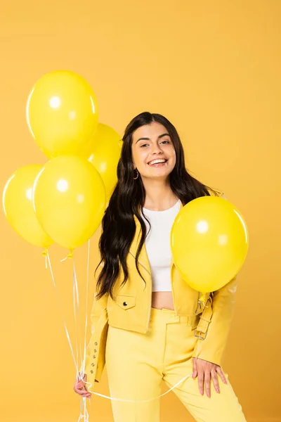 Brunette young woman holding yellow balloons, isolated on yellow — Stock Photo
