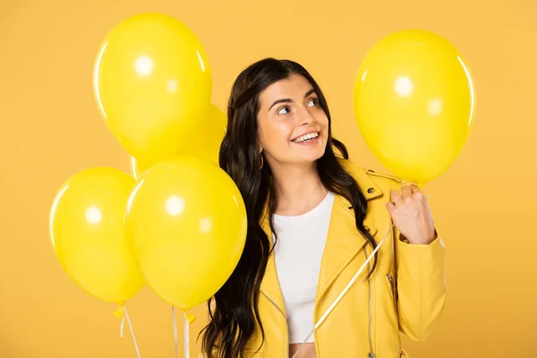 Alegre chica sosteniendo globos amarillos, aislado en amarillo - foto de stock