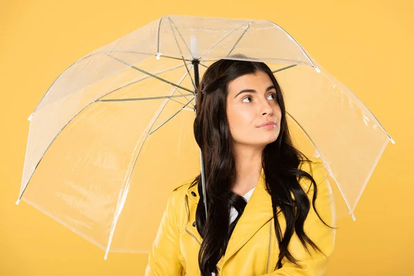 Bela mulher pensativa posando com guarda-chuva transparente, isolado no amarelo — Fotografia de Stock