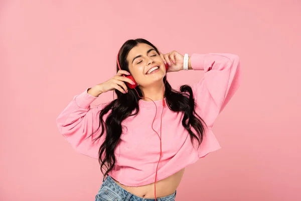 Mujer feliz escuchando música con auriculares, aislado en rosa - foto de stock