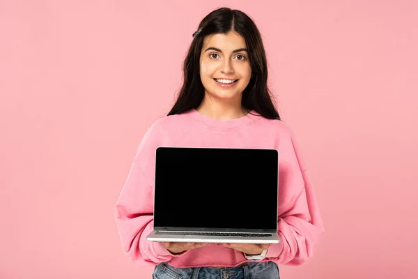Весела дівчина, що показує ноутбук з порожнім екраном, ізольована на рожевому — стокове фото
