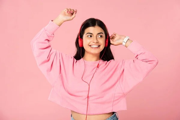 Красива дівчина танцює і слухає музику з навушниками, ізольована на рожевому — стокове фото