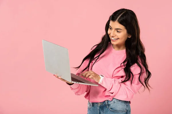 Красива усміхнена дівчина використовує ноутбук, ізольований на рожевому — стокове фото
