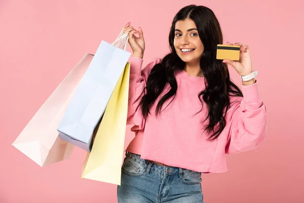 Atractiva chica con tarjeta de crédito y bolsas de la compra, aislado en rosa - foto de stock