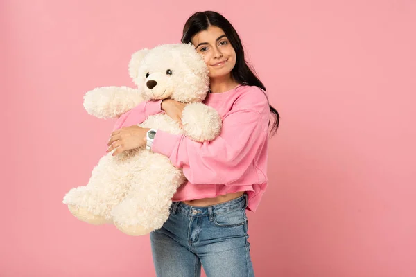Приваблива дівчина обіймає плюшевого ведмедя, ізольована на рожевому — стокове фото
