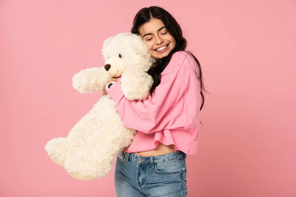 Lächelnde junge Frau umarmt Teddybär, isoliert auf rosa — Stockfoto
