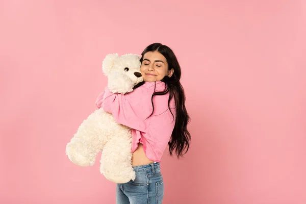Linda menina feliz abraçando ursinho de pelúcia, isolado em rosa — Fotografia de Stock