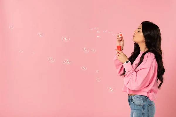 Attraktives Mädchen bläst Seifenblasen isoliert auf rosa — Stockfoto