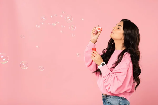 Mujer alegre soplando burbujas de jabón aislado en rosa - foto de stock