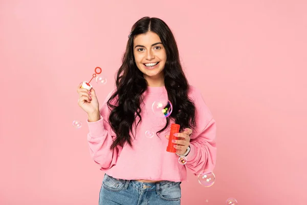 Sorridente giovane donna soffiando bolle di sapone isolato su rosa — Foto stock