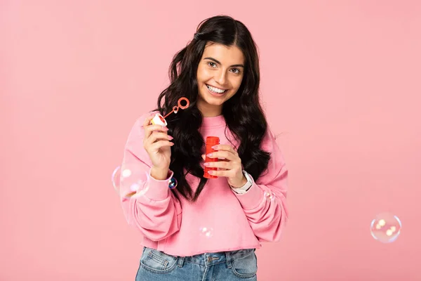 Красива усміхнена молода жінка грає з мильними бульбашками ізольована на рожевому — стокове фото