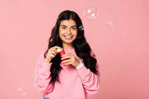 Привлекательная счастливая молодая женщина играет с мыльными пузырями изолированы на розовый — стоковое фото