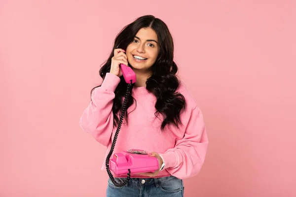 Lächelndes attraktives Mädchen, das am Retro-Telefon isoliert auf rosa spricht — Stockfoto