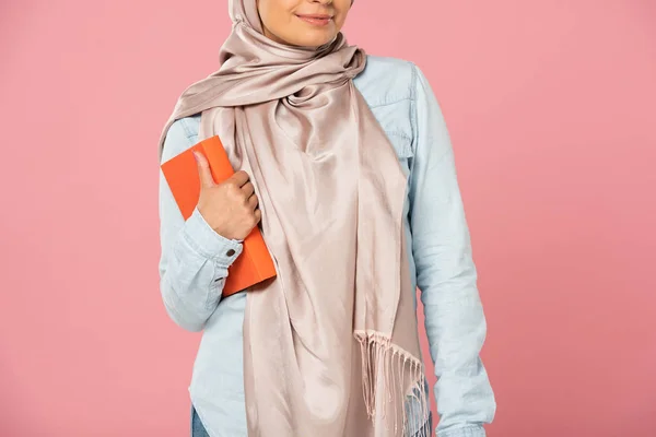 Vue recadrée de l'étudiant musulman en hijab tenant livre isolé sur rose — Photo de stock