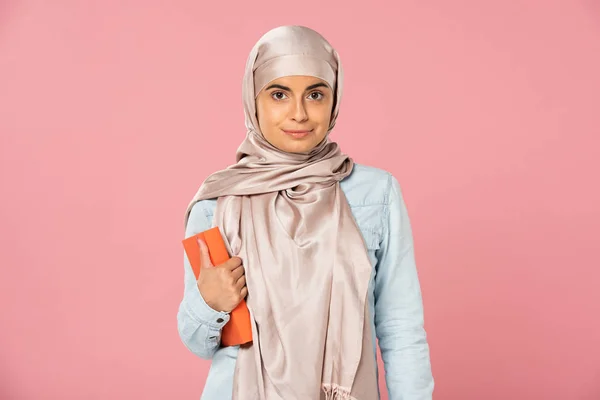 Hermoso musulmán estudiante en hijab celebración libro aislado en rosa - foto de stock