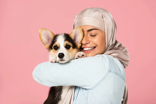 Fröhliche arabische Frau im Hijab mit walisischem Corgi-Welpen, isoliert auf rosa — Stockfoto