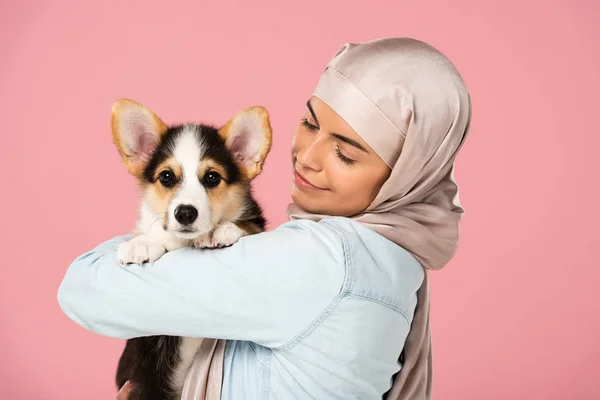 Happy muslim girl in hijab holding cute puppy, isolated on pink — Stock Photo