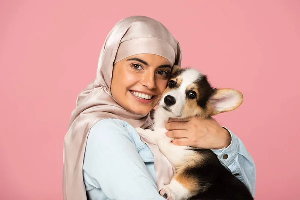 Muslim girl in traditional scarf holding little puppy, isolated on pink — Stock Photo