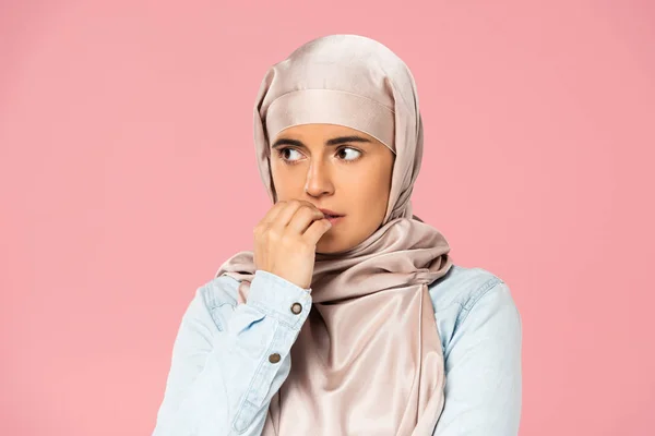 Chica musulmana asustada en hijab mordiendo clavos, aislado en rosa - foto de stock