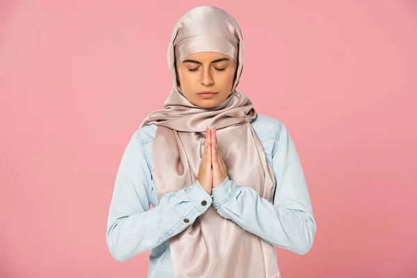 Atractiva chica musulmana en hijab orando con los ojos cerrados, aislado en rosa - foto de stock