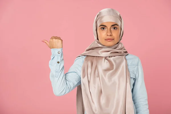 Belle fille musulmane en hijab montrant quelque chose avec pouce, isolé sur rose — Photo de stock