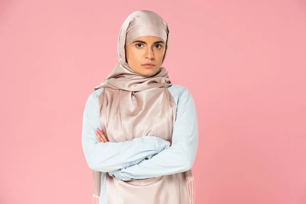 Attractive skeptical arabic girl in hijab with crossed arms, isolated on pink — Stock Photo