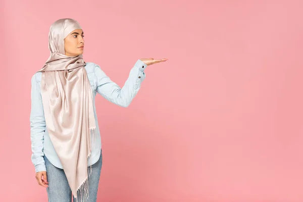 Belle femme musulmane en hijab montrant quelque chose, isolé sur rose — Photo de stock