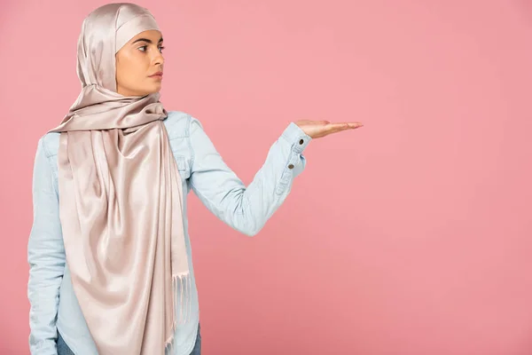 Bela mulher muçulmana em hijab apresentando algo, isolado em rosa — Fotografia de Stock