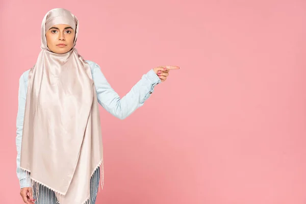 Mujer musulmana en hiyab apuntando a algo, aislada en rosa - foto de stock