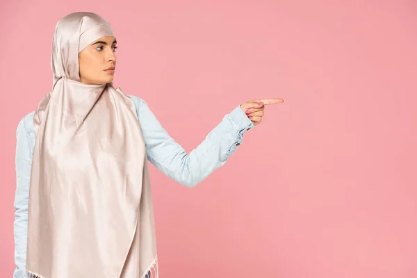 Bela mulher islâmica em hijab mostrando algo, isolado em rosa — Fotografia de Stock