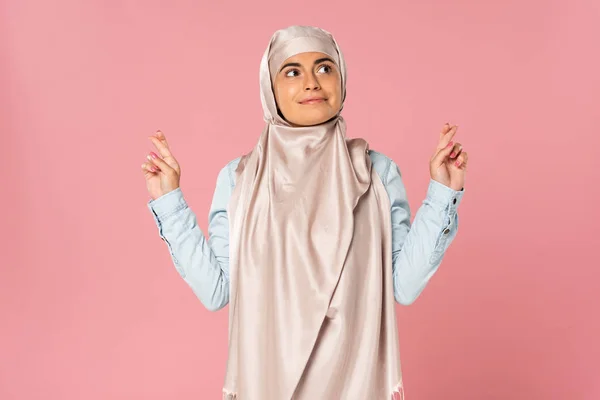 Heureuse femme musulmane en hijab avec les doigts croisés, isolée sur rose — Photo de stock